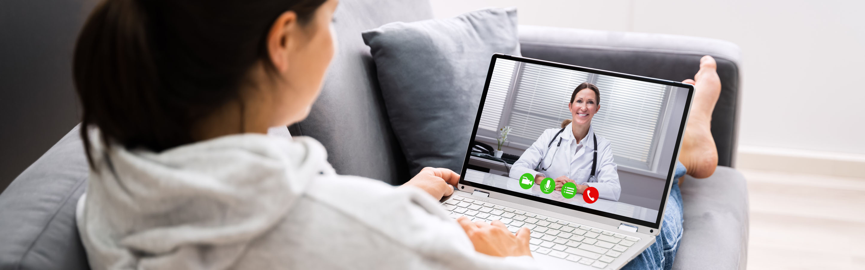 woman sitting on a couch holding a laptop having a video visit with a doctor